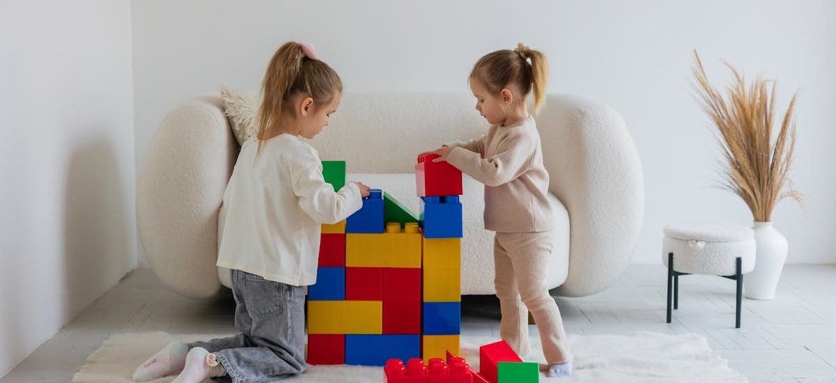 Two young girls enjoying a playful activity with large colorful blocks in a cozy living room.