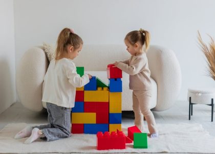 Two young girls enjoying a playful activity with large colorful blocks in a cozy living room.